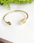 Angelco Accessories hammered coin cuff - gold - flatlay on white board with green fern