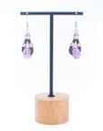 Angelco Accessories Ceramic bead cork drop earrings in purple, presented on hanging stand