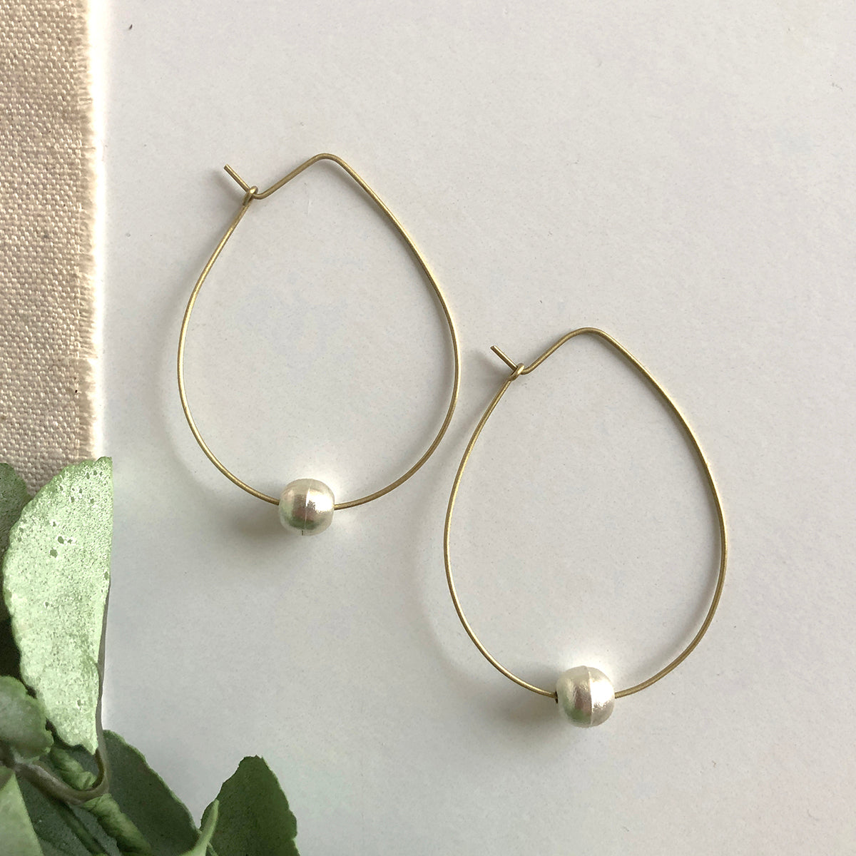Angelco Accessories Floating pearl hoop earrings - on white flatlay with linen and green leaves