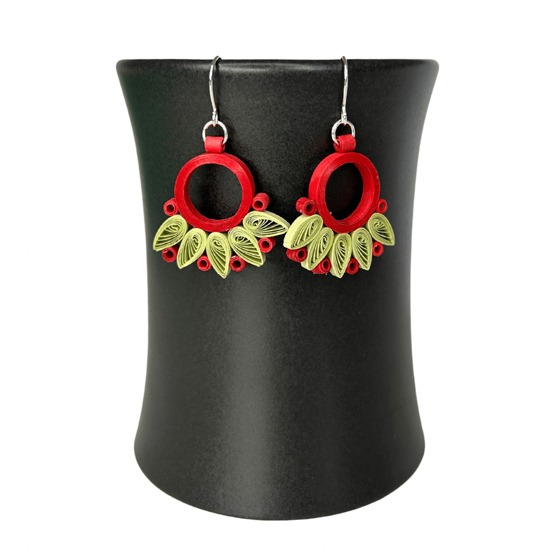 Angelco Accessories Paper bloom earrings of red and green, hanging on a ceramic cup on a white background
