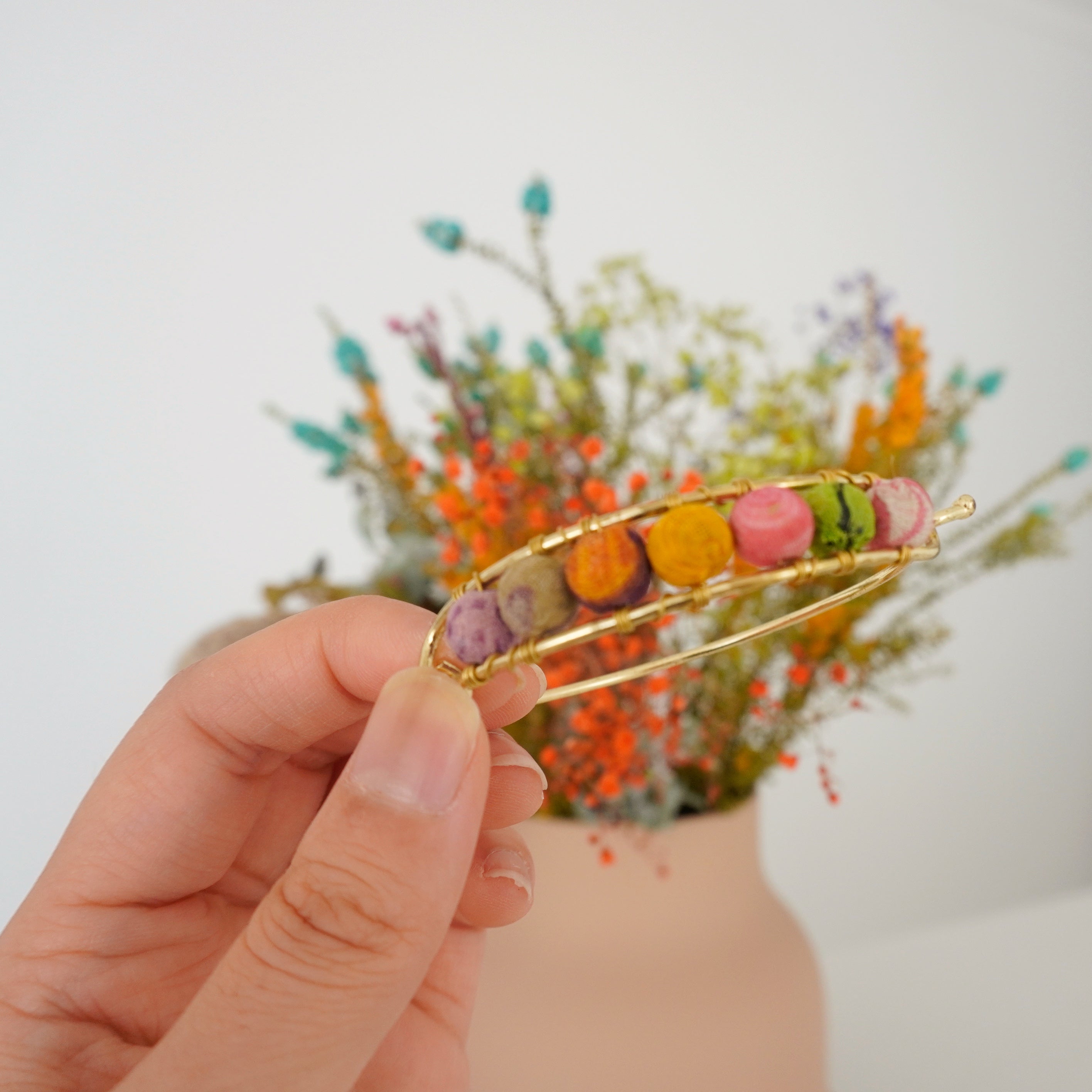 Angelco Accessories Kantha gold bangle - close up of bangle held by models hand with flower background