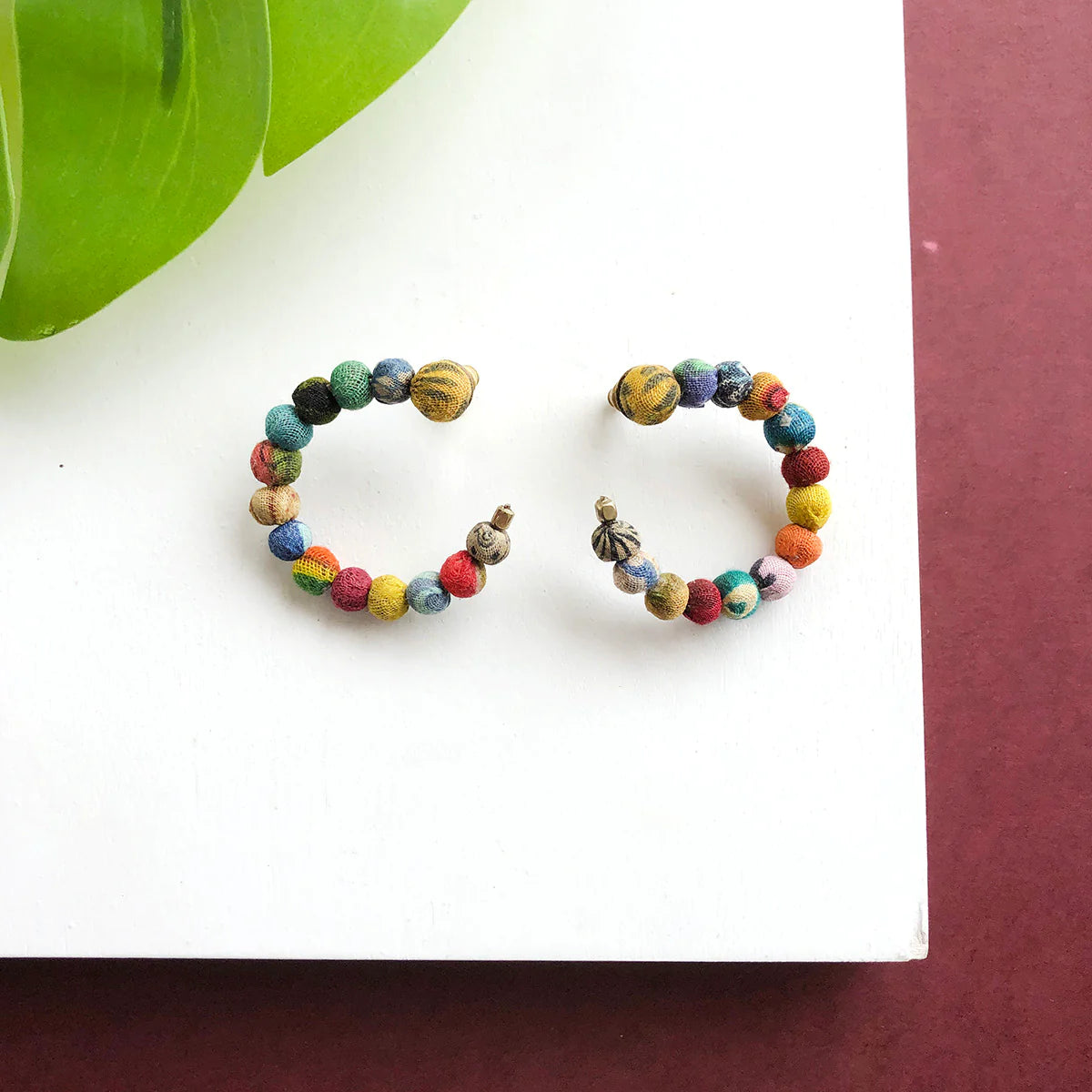 Angelco Accessories flatlay kantha hoop earrings  on white and brown background with green leaf