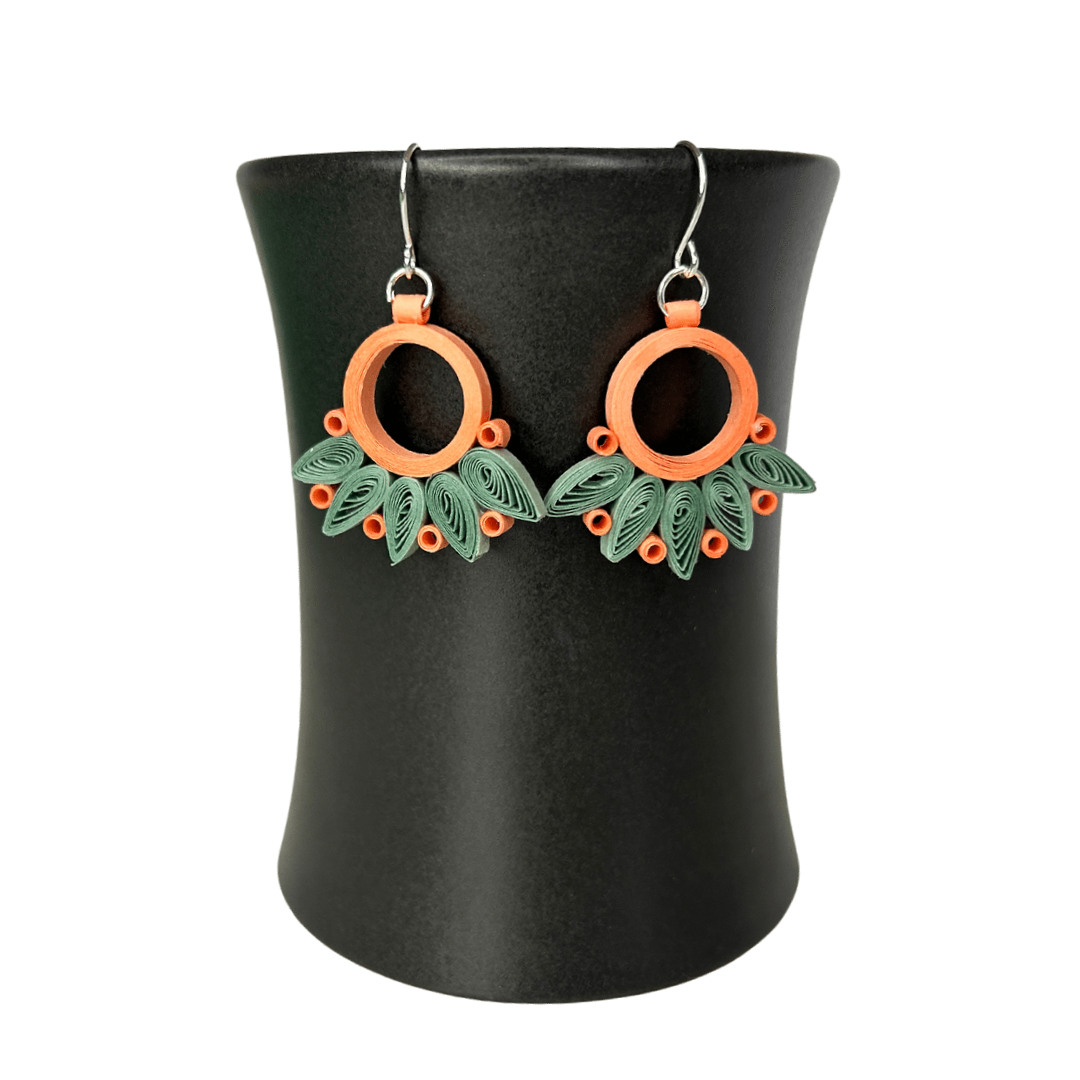 Angelco Accessories Paper bloom earrings of orange and green, hanging on a ceramic cup on a white background