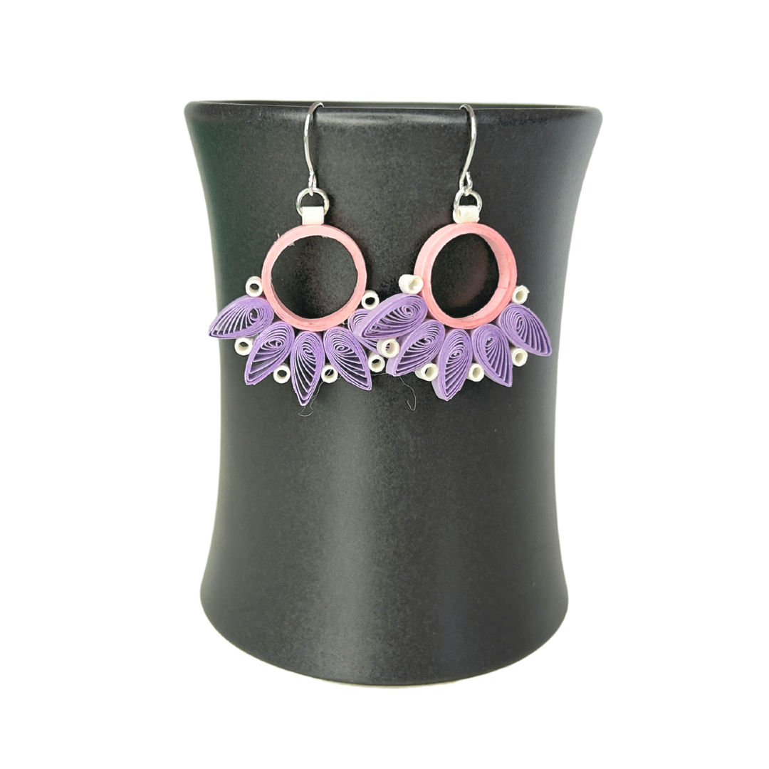 Angelco Accessories Paper bloom earrings of pink and purple, hanging on a ceramic cup on a white background