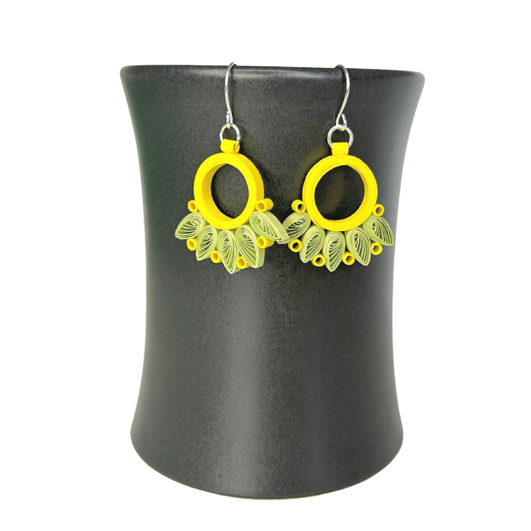 Angelco Accessories Paper bloom earrings of yellow and green, hanging on a ceramic cup on a white background