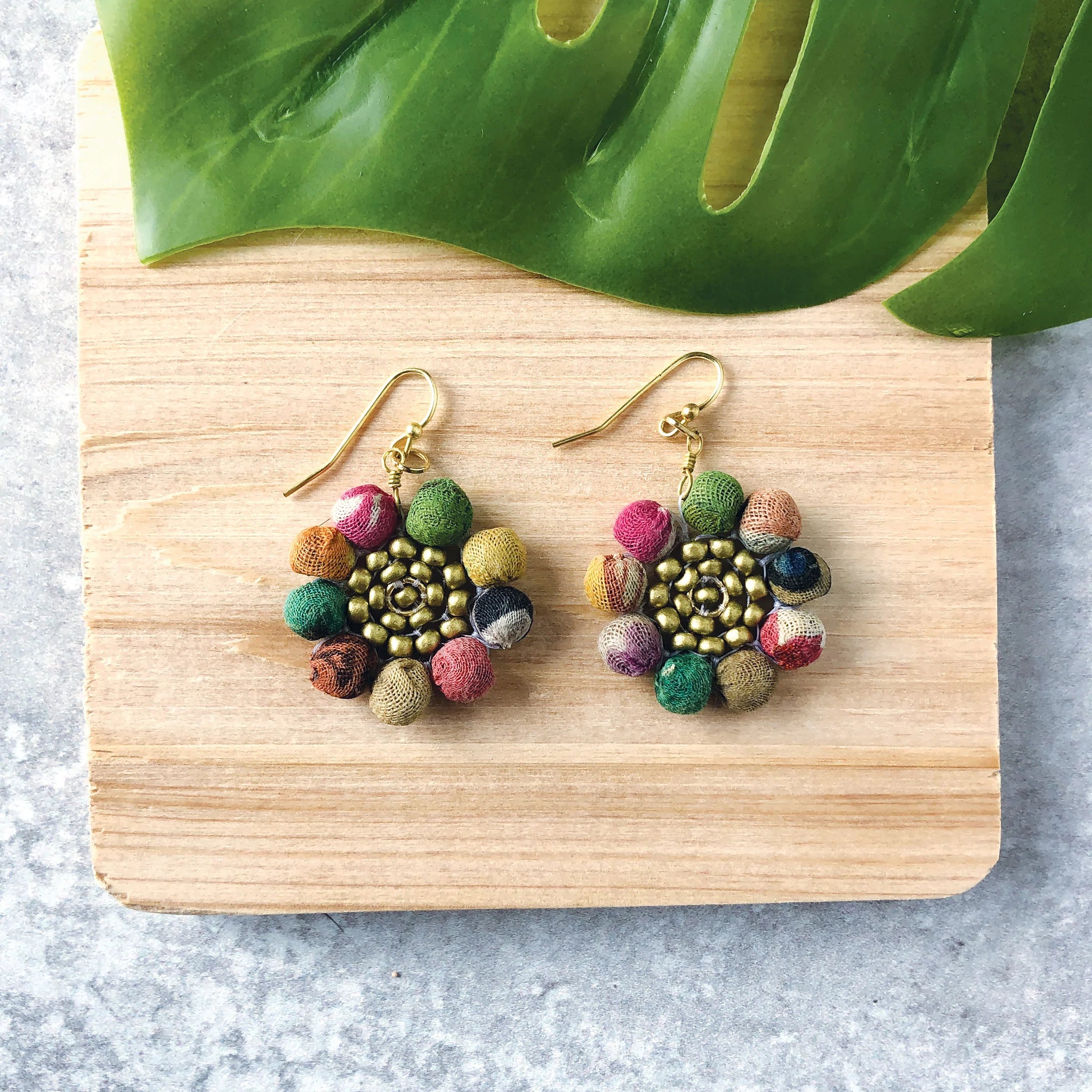 Angelco Accessories Sunny flower kantha earrings flat-laid on a wooden board with leaf